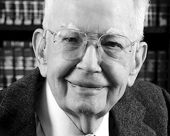 Ronald Coase headshot in front of a bookcase
