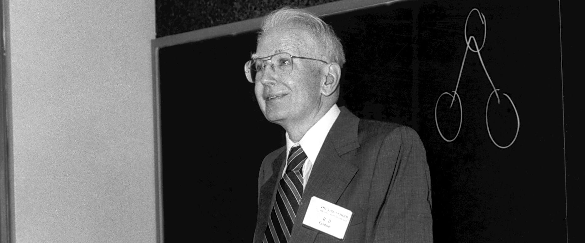 Ronald Coase standing in front of a blackboard