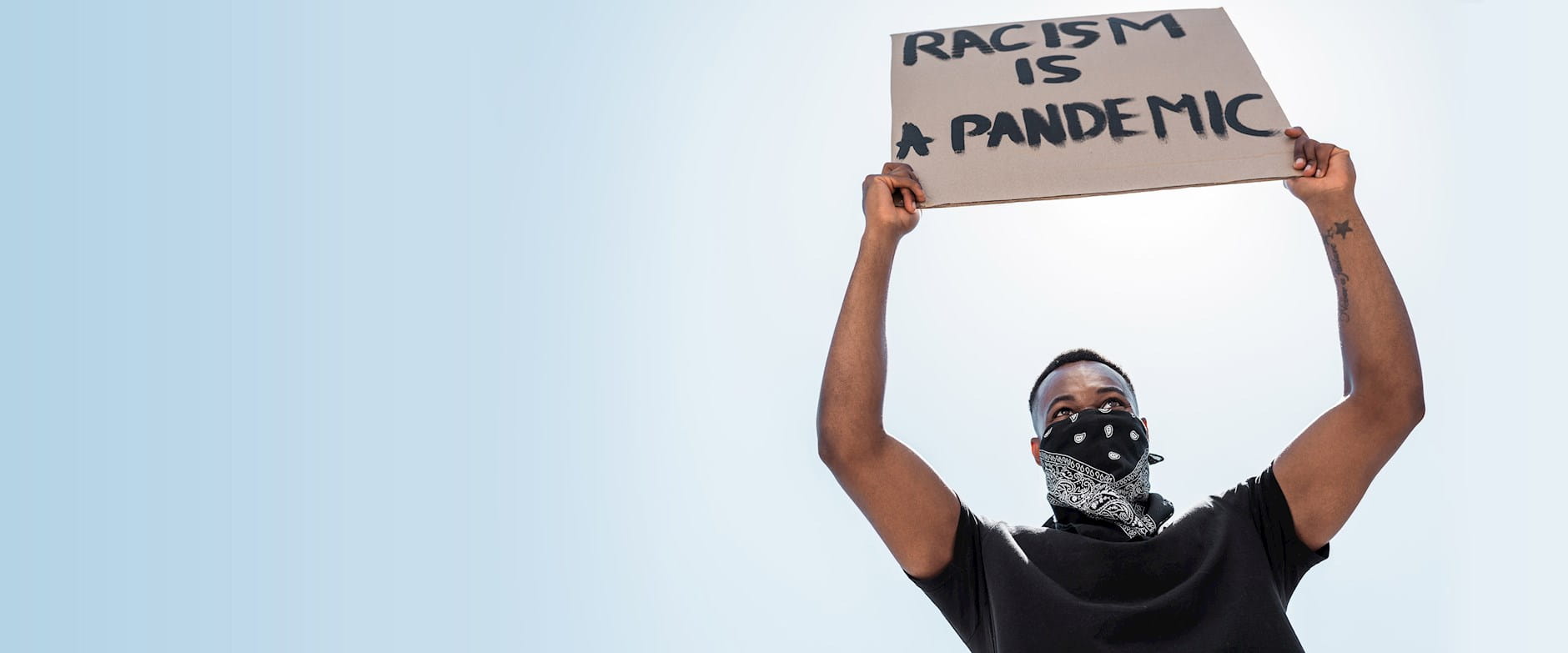 A masekd man at a rally holding a sign above his head that reads "Racism is a pandemic"