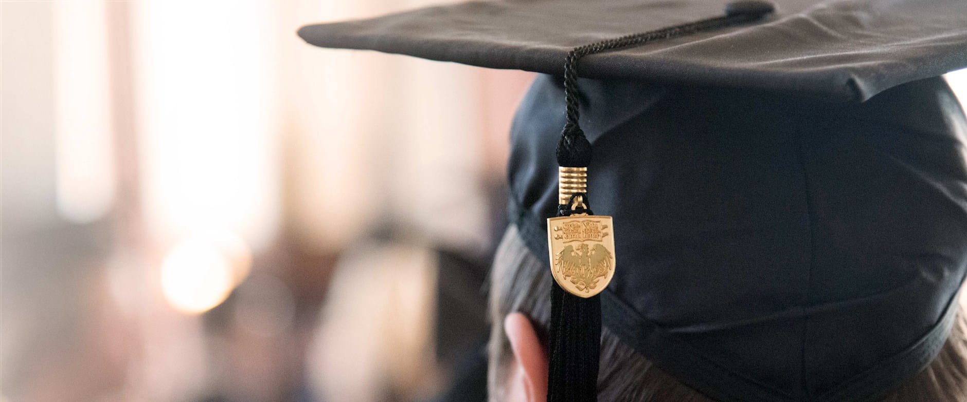 Close-up of a Chicago Booth graduation cap with gold university seal visibile on the tassel; the hat is being worn by a graduate